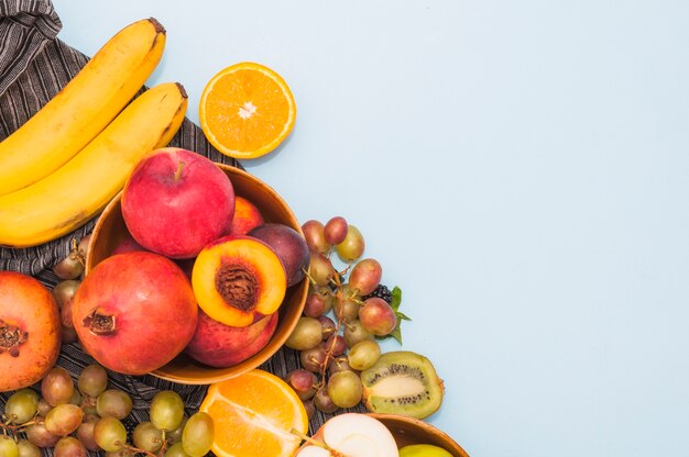 An overhead view of fruits; banana; grapes; kiwi and peach on blue background