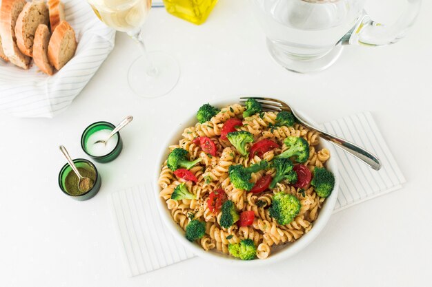 An overhead view of fusilli pasta with vegetables on white background