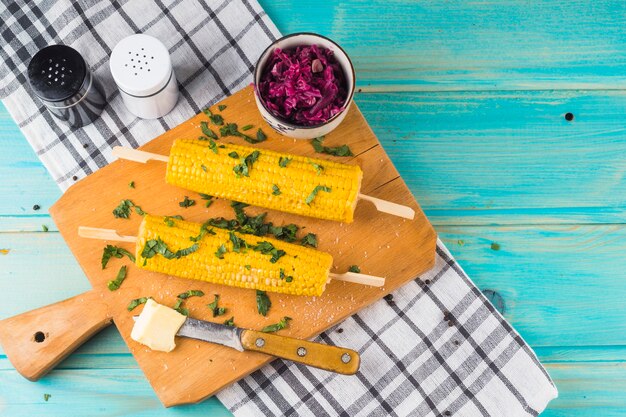 Overhead view of a garnish corn with butter on wooden chopping board