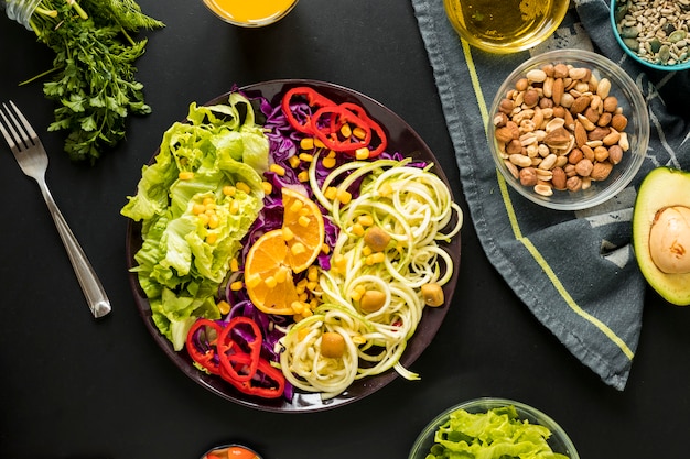 Overhead view of garnished healthy salad in plate with drifts and fork against black background