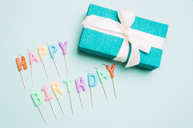 Free Photo an overhead view of gift box and happy birthday candles with stick on blue backdrop
