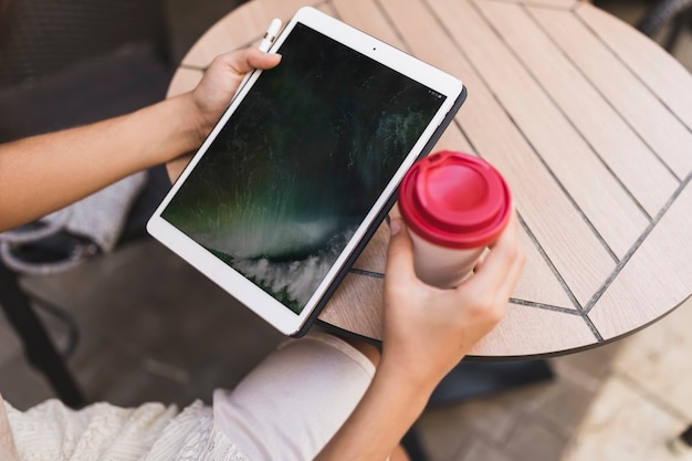 Una vista aerea di una ragazza che tiene compressa digitale e tazza di caffè da asporto sul tavolo