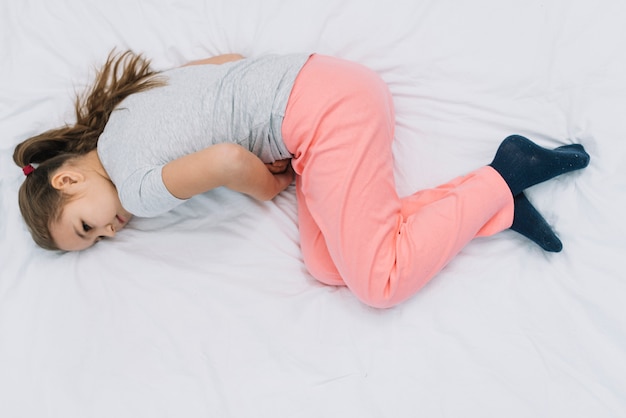 An overhead view of a girl lying on bed suffering from stomach ache