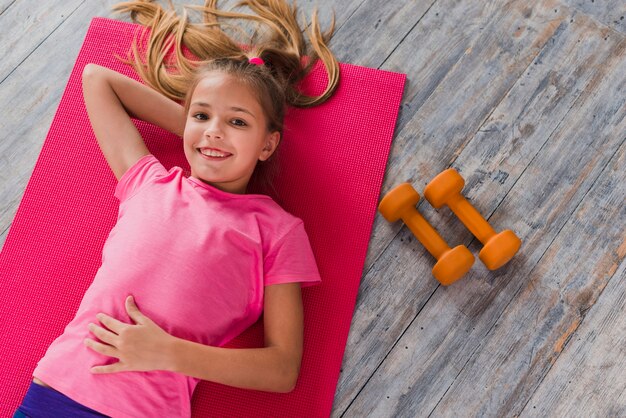 An overhead view of a girl lying on exercise mat near the dumbbell