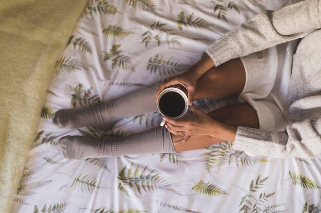 An overhead view of a girl sitting on bed wearing socks holding coffee cup