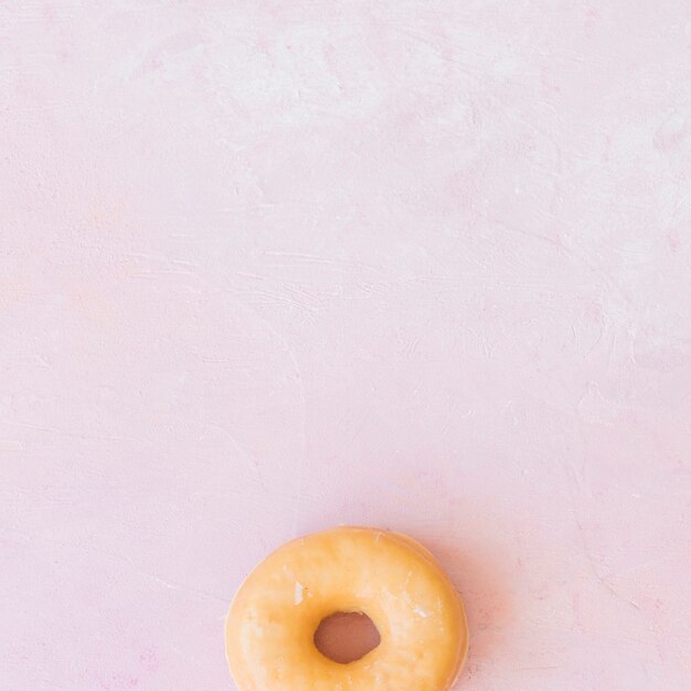 Overhead view of glazed donut on pink background