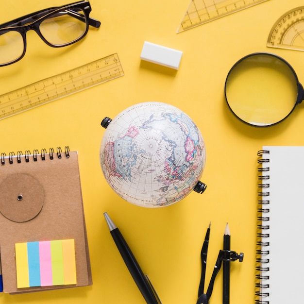 Free photo overhead view of globe with various equipments on yellow background