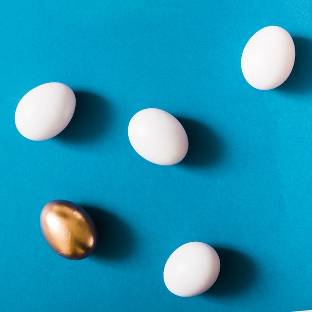 Overhead view of golden egg among the white eggs on blue background