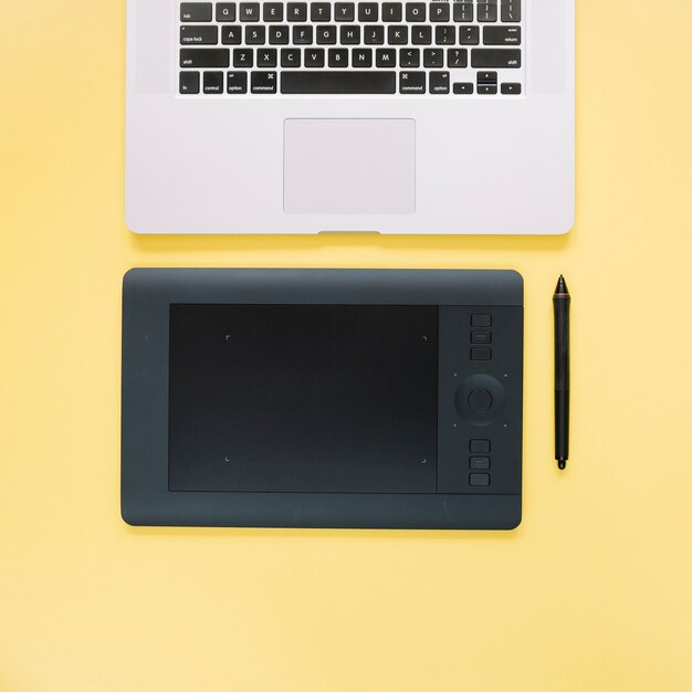 Вид сверху графического цифрового планшета и ноутбука на желтой поверхности