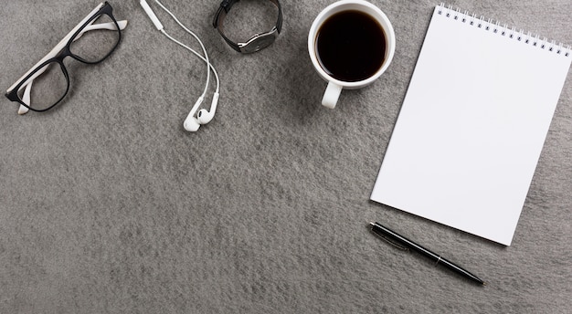 An overhead view of gray table desk with office supplies; personal accessories and coffee cup