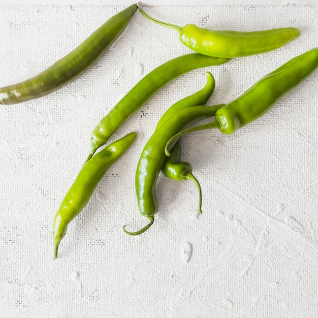 Free photo an overhead view of green chilies on white texture backdrop