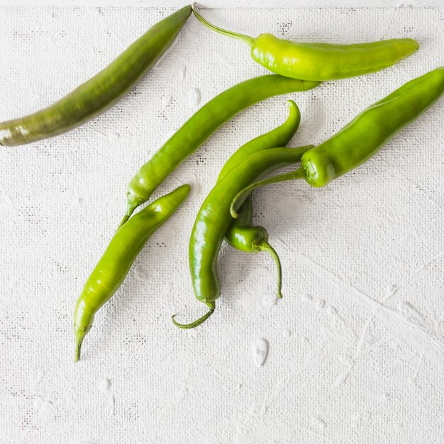 An overhead view of green chilies on white texture backdrop