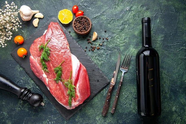 Free photo overhead view of green on fresh red raw meat on cutting board and pepper lemon black hammer flower wine bottle on green black mix color background