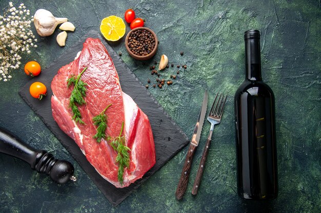 Overhead view of green on fresh red raw meat on cutting board and pepper lemon black hammer flower wine bottle on green black mix color background