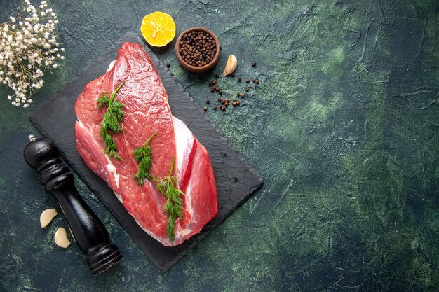 Overhead view of green on fresh red raw meat on cutting board and pepper lemon wooden hammer flower on the right side on green black mix color background