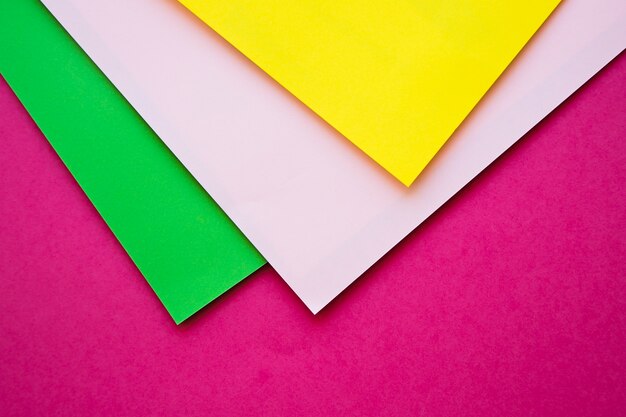 Overhead view of green; grey and yellow cardboard papers on pink surface