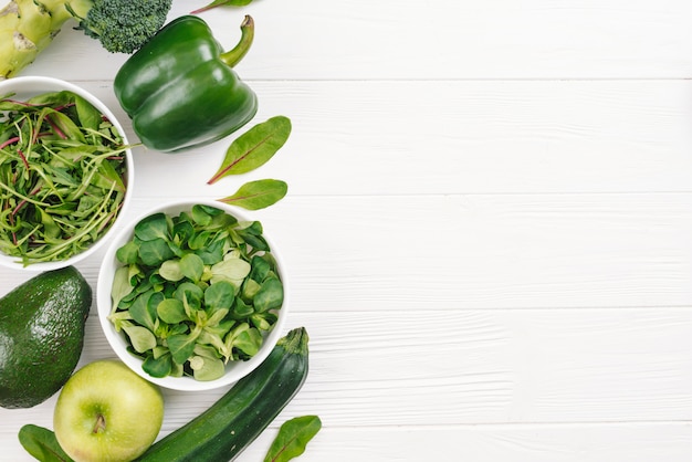 An overhead view of green healthy fresh vegetables on white wooden desk