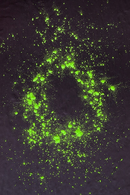 Free photo an overhead view of green holi powder splatter on dark background