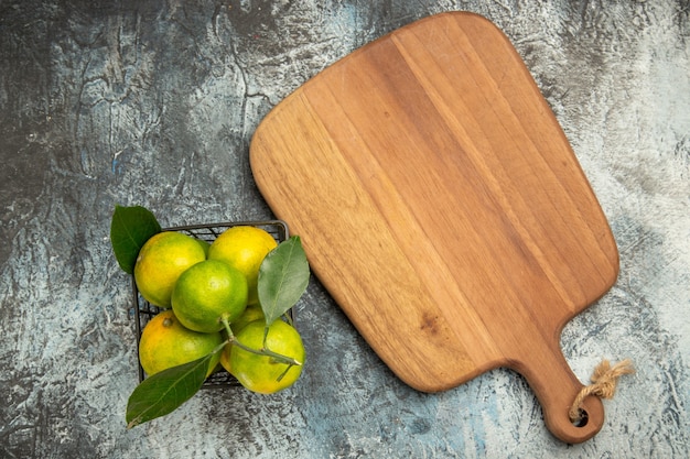 Overhead view of green mandarins with leaves in a basket and cutting board on gray background