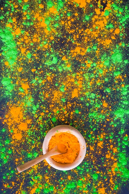 An overhead view of green and orange splatter holi powder with bowl