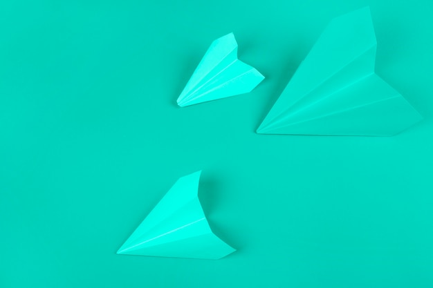 An overhead view of green paper airplanes on mint background