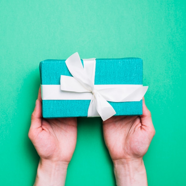 An overhead view of green wrapped gift bow with white ribbon bow on green backdrop