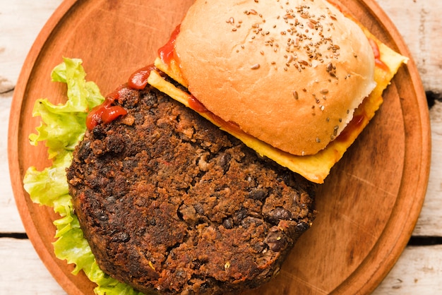 An overhead view of hamburger with cheese; tomatoes and lettuce on wooden chopping board