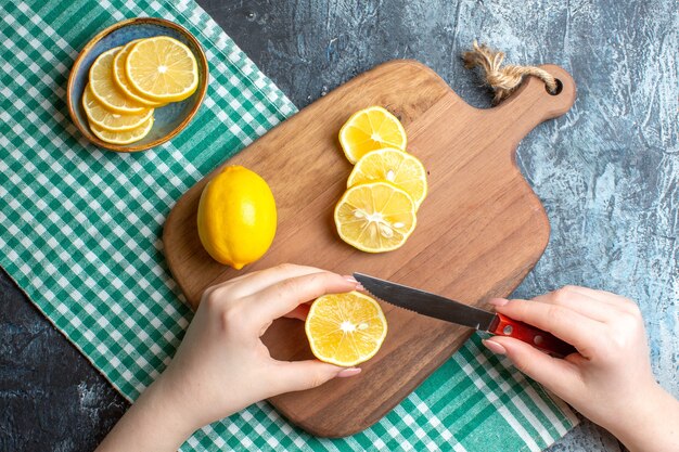 Overhead view of a hand chopping fresh lemons on a wooden cutting board on dark background