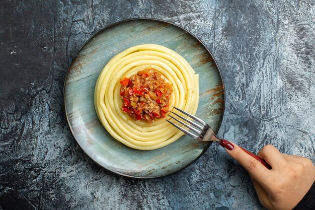 Вид сверху руки, держащей вилку на вкусной пасте на синей тарелке, подается с помидорами и мясом на ужин