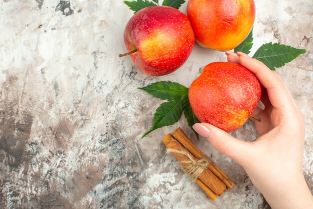 混合色の背景に新鮮な天然の赤いリンゴとシナモンライムの1つを持っている手の俯瞰図