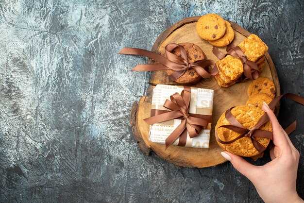 Overhead view of hand holding one of various delicious cookies on wooden cutting board on the left side on dark icy background