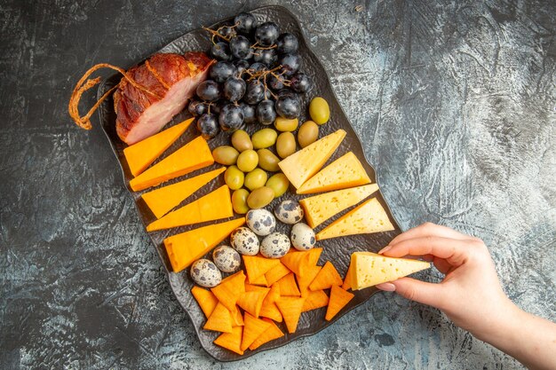Overhead view of hand taking one of foods from delicious best snack for wine on brown tray on ice background