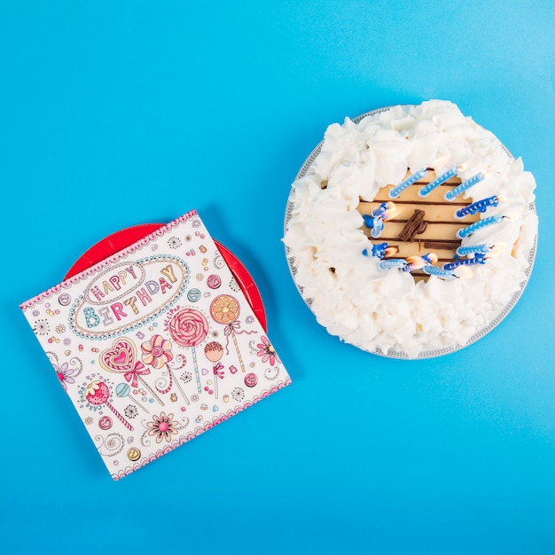 An overhead view of happy birthday card on plate with birthday cake against blue background