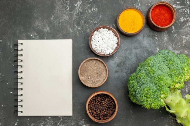 Overhead view of healthy meal with broccoli on a black plate and spices with notebook