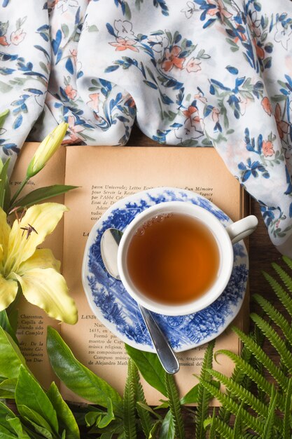 Una vista dall'alto della tazza di tisana sul libro con foglie verdi; tovaglia e fiore di giglio giallo