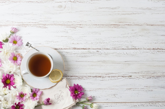 An overhead view of herbal tea cup with flowers on painted wooden textured backdrop