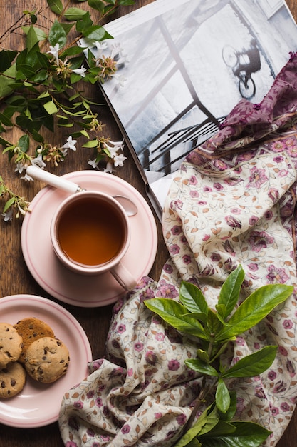 An overhead view of herbal tea with cookies; twigs; book and scarf on table