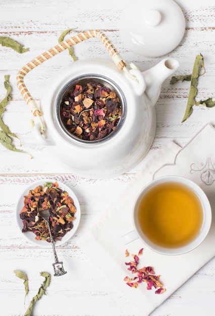An overhead view of herbal tea with dried rose petals on wooden desk