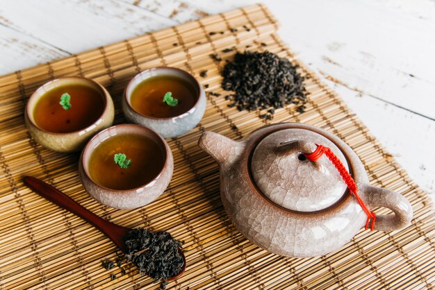 An overhead view of herbal teacups and teapot with dried tea leaves on placemat