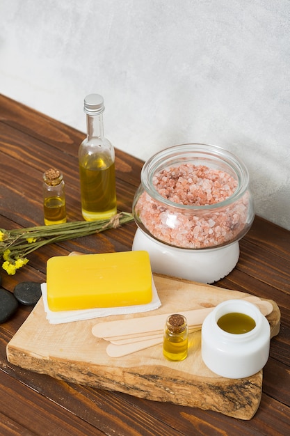 An overhead view of himalayan salt jar; herbal soap; lastone; essential oil; honey and limonium flowers on table