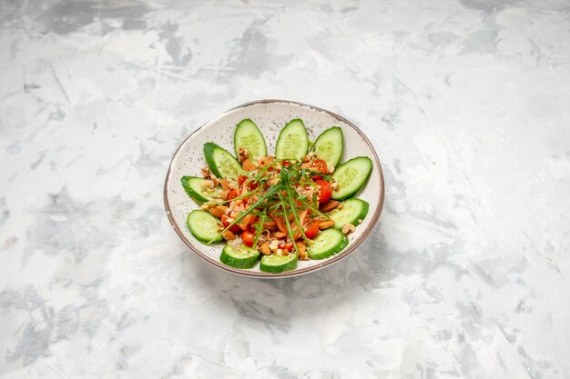 Overhead view of homemade healthy delicious vegan salad decorated with chopped cucumbers in a bowl on stained white surface with free space