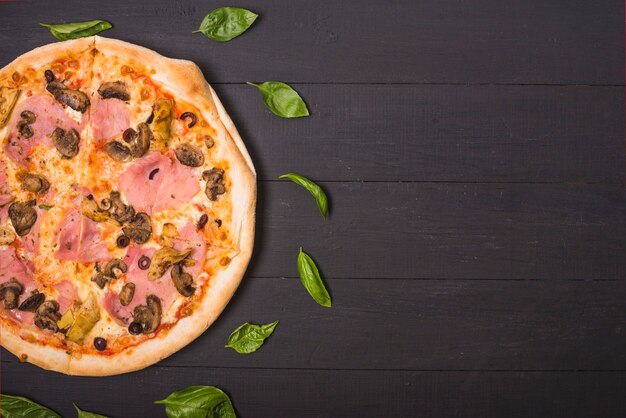 An overhead view of homemade pizza decorated with basil leaves on wooden plank