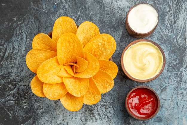 Overhead view of homemade potato chips decorated like flower shaped and salt with ketchup mayonnaise on gray table