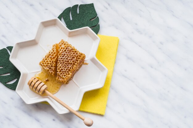 An overhead view of honeycomb with wooden dipper on tray over the white marble