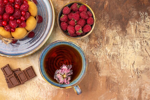 Overhead view of hot herbal tea soft cake with fruits chocolate bars on mixed color table