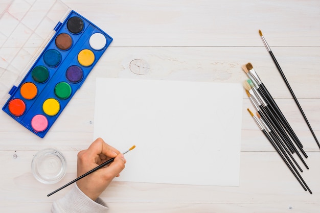 Free photo overhead view of human hand painting on white blank paper with paint brush