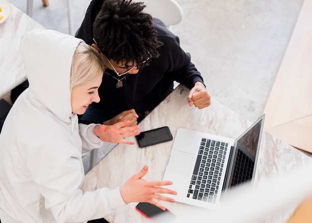 An overhead view of interracial young couple cheering after looking at laptop on table