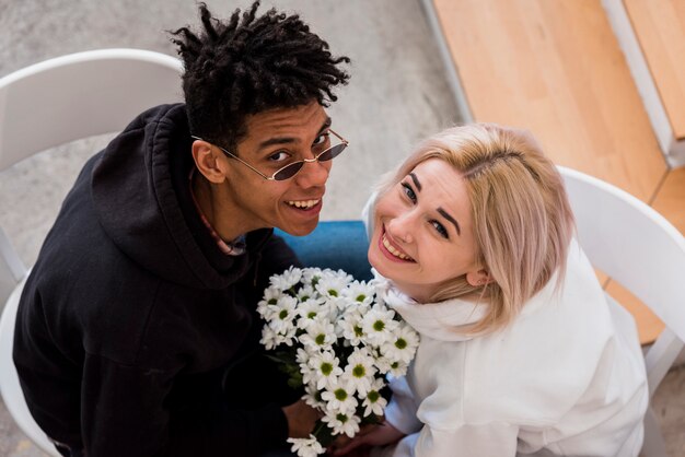 An overhead view of interracial young couple holding white flower in hand looking up