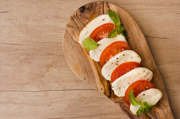 An overhead view of italian caprese salad with slices of mozzarella cheese; basil and tomatoes on serving board