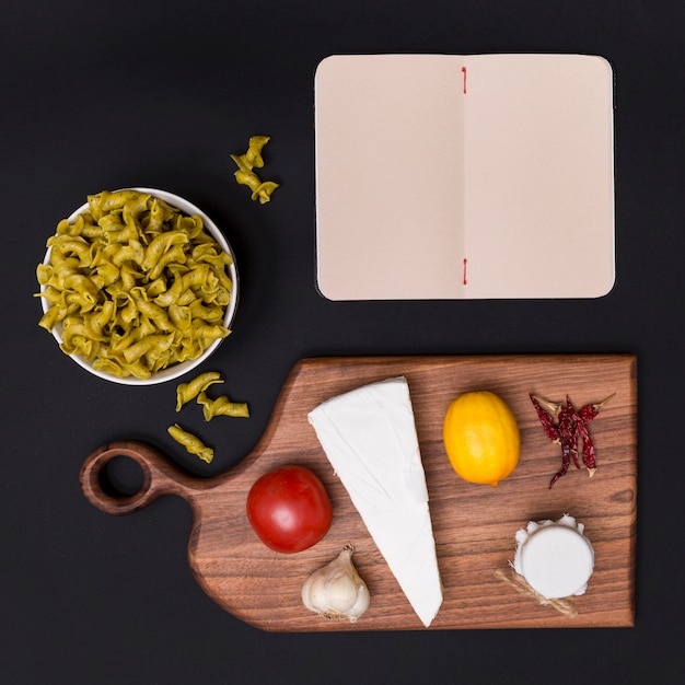 Overhead view of italian raw pasta; healthy ingredient; cutting board and blank diary over black backdrop